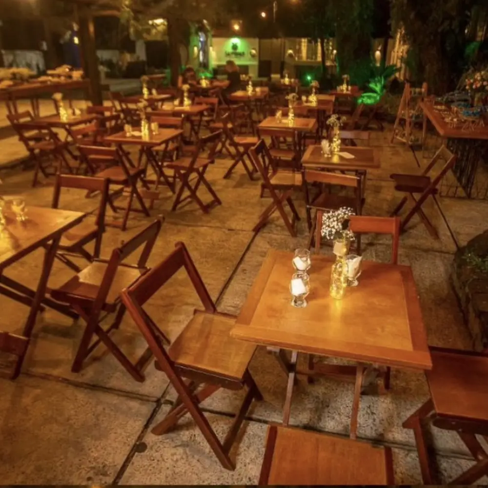 Área de mesas do espaço de eventos em Uruguaiana iluminada à noite, cercada pelo verde