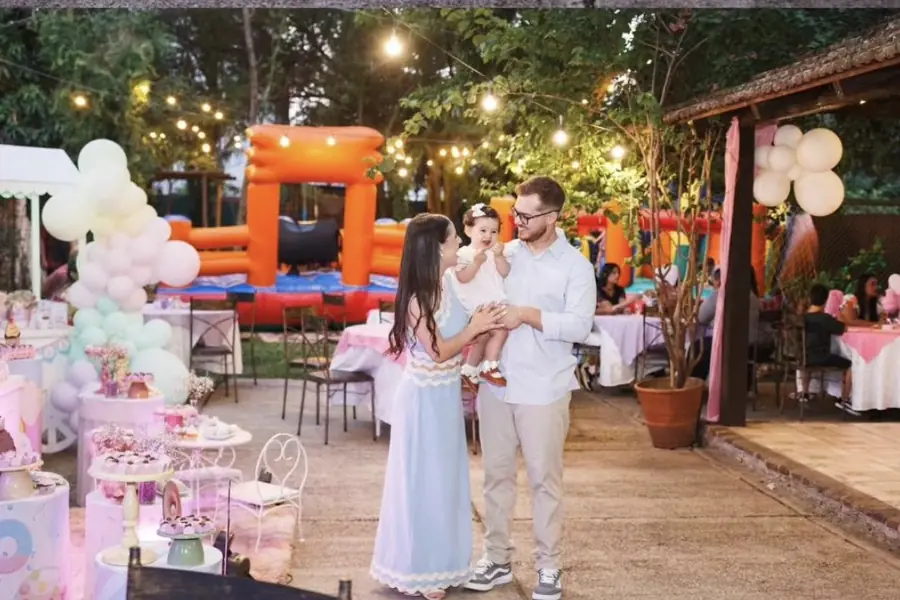Família com o bebê em festa infantil, com pula-pula do espaço kids ao fundo, em Uruguaiana